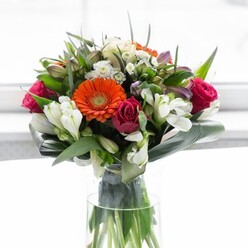 Encapsulating the artistry of a Yeading florist, this exquisitely crafted bouquet brings together an array of complementary tones and textures. Creamy peach gerbera daisies form a subtle halo, surrounding electric orange centers that radiate warmth and cheerfulness. Deep fuchsia roses punctuate the display, adding a dramatic sophistication, while elegant white alstroemeria and petite white flowers intersperse brightness and fine detail throughout the arrangement. Large, glossy aspidistra leaves wrap securely around the base, their rich green arcs evoking the tranquil garden corners in Yeading's tree-lined avenues, while finer green sprigs emerge playfully between the blooms. Each flower is gently illuminated by soft daylight, ensuring the natural vibrancy of every hue is beautifully enhanced. A clear, slender vase reveals the vital green stems, heightening the arrangement's fresh-from-the-garden feel. The subtle scent-notes of rose mingled with the crispness of lily-lingers in the air, conjuring the essence of early mornings explored along Yeading Brook. This bouquet is poised for celebrations, thoughtful gifts, or simply as a vibrant focal point in a welcoming home. Created with expert care by Flowers Yeading, it exudes optimism, connection, and the signature artistry of your local flower shop.